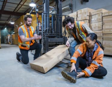 An industrial warehouse workplace safety topic. A worker injured falling or being struck by a forklift.